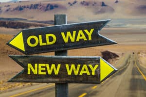 Two wooden signposts with yellow arrows stand against a desert backdrop. The top sign points left and reads "OLD WAY," while the bottom sign points right and reads "NEW WAY." In the distance, a road stretches towards barren hills, reminiscent of finding "CPAs near me" for financial guidance.