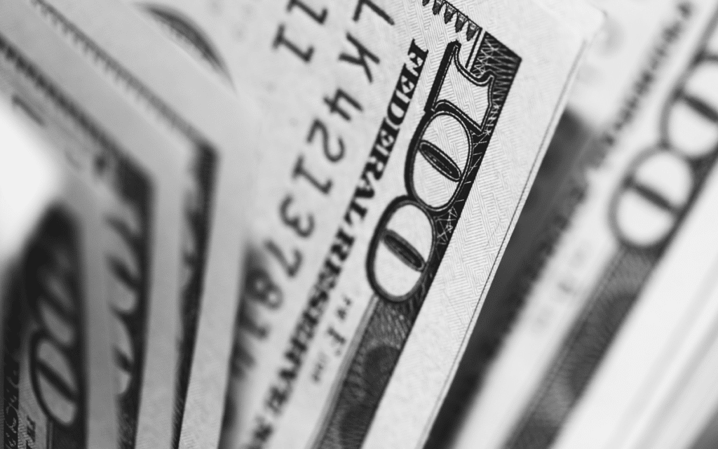 Close-up image of several U.S. hundred-dollar bills, showing the intricate details of the "100" text and part of Benjamin Franklin's face on the front of one bill, with other bills slightly blurred in the background. Such images are often meticulously analyzed by tax accountants to ensure financial accuracy.