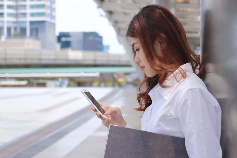 Close up young Asian employee woman using mobile phone in her hands for job at outside office.